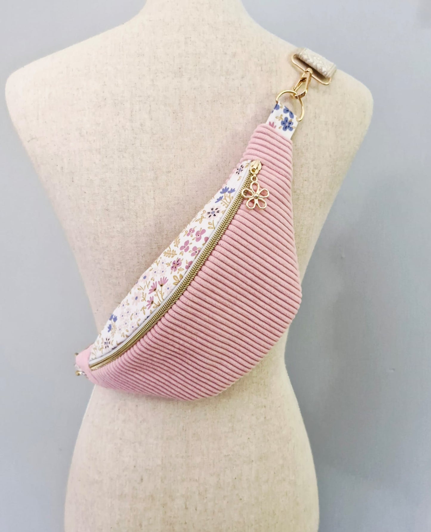 Sac banane fait main en velours côtelé rose bonbon avec bande supérieure à motif fleuri, sangle beige réglable et pendentif doré, présenté sur mannequin et à plat.
