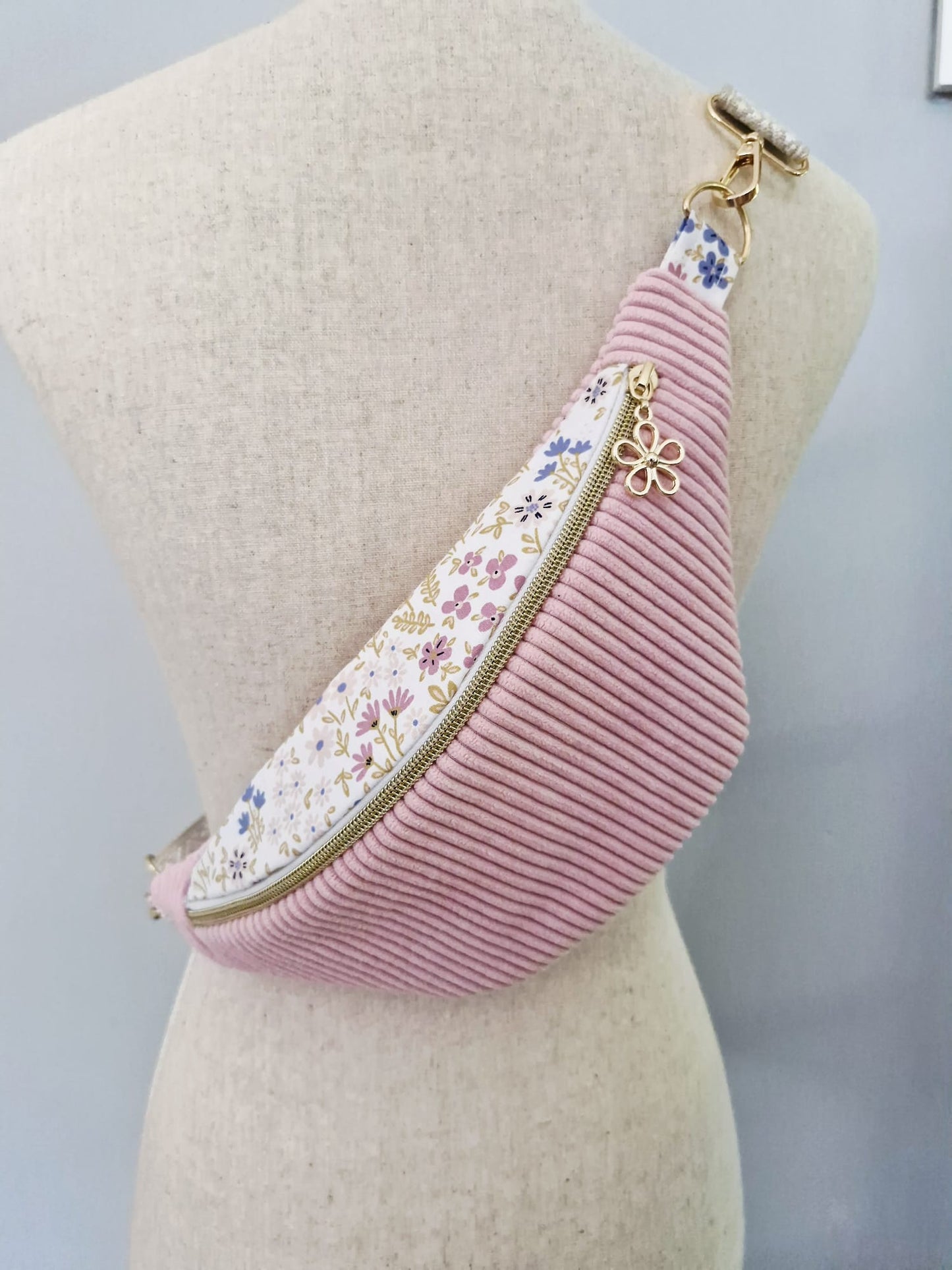 Sac banane fait main en velours côtelé rose bonbon avec bande supérieure à motif fleuri, sangle beige réglable et pendentif doré, présenté sur mannequin et à plat.