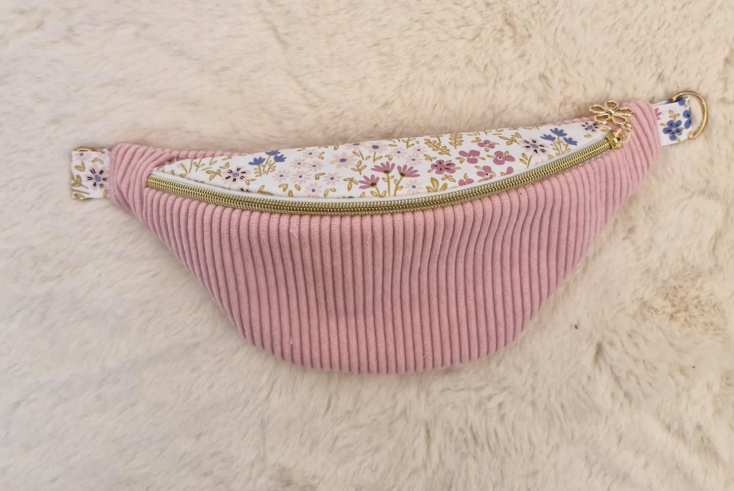 Sac banane fait main en velours côtelé rose bonbon avec bande supérieure à motif fleuri, sangle beige réglable et pendentif doré, présenté sur mannequin et à plat.