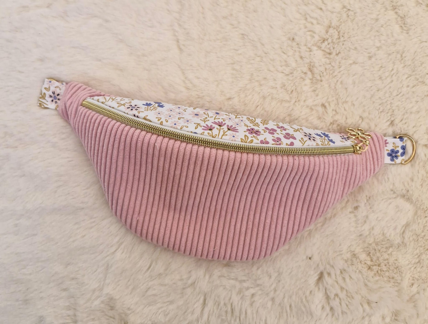 Sac banane fait main en velours côtelé rose bonbon avec bande supérieure à motif fleuri, sangle beige réglable et pendentif doré, présenté sur mannequin et à plat.
