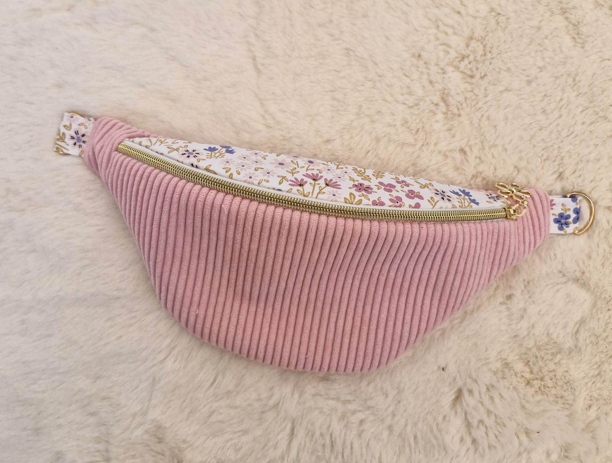Sac banane fait main en velours côtelé rose bonbon avec bande supérieure à motif fleuri, sangle beige réglable et pendentif doré, présenté sur mannequin et à plat.